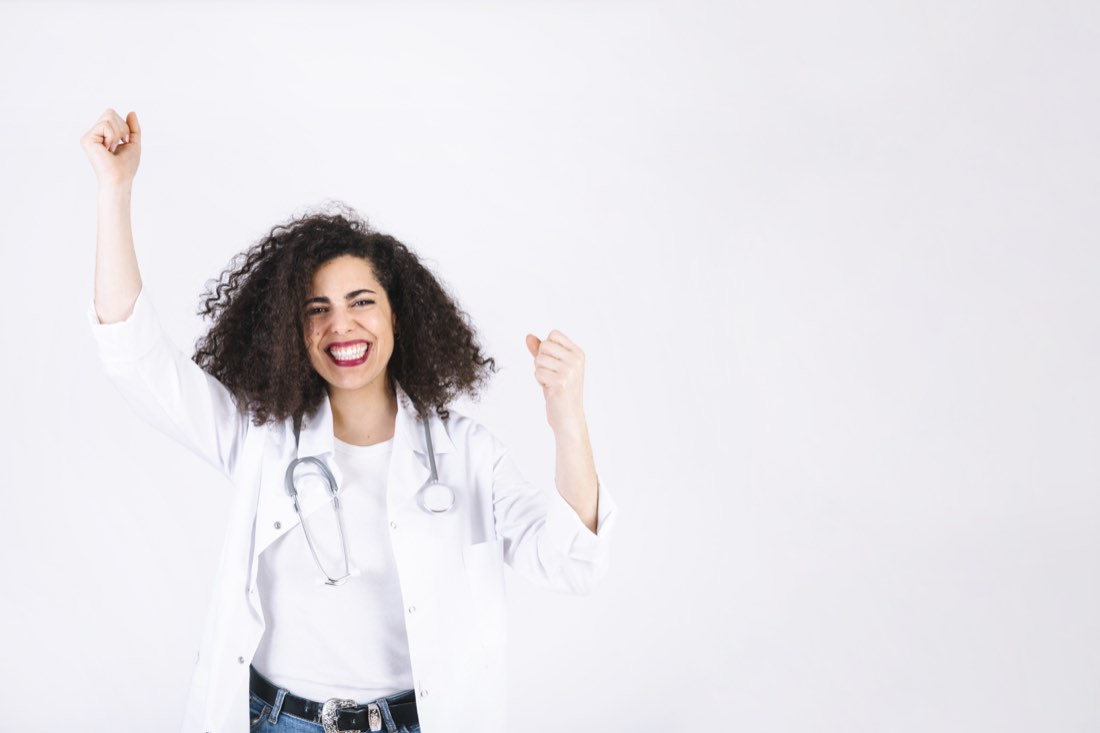 Jovem médica de jaleco branco comemorando com os punhos erguidos